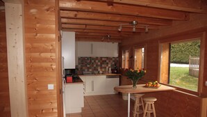 Cucina di una baita in legno con mobili bianchi, zoccolo piastrellato e una finestra con vista su del verde.