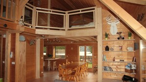 Un'ampia baita in legno con zona pranzo, camera da letto in soppalco e soggiorno con divano.