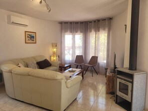 Een woonkamer met een bank, stoelen, een tafel, een open haard en een raam met gordijnen.