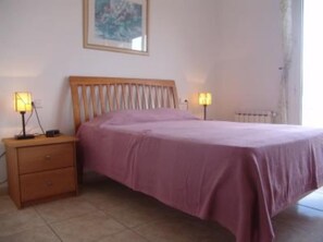 Un dormitorio con cama, mesita de noche, lámpara y un cuadro en la pared.