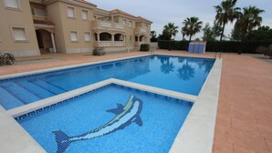 A swimming pool with a dolphin mosaic, a building with balconies, and palm trees. - AP ECODUNES, Ideal house for your holidays near the sea, free wifi, optional air conditioning, community pool, pets allowed, dog’s beach (Delta de l'ebre)