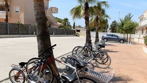 A row of bicycles parked on a sidewalk with a palm tree and a car in the background. - AP ECODUNES, Ideal house for your holidays near the sea, free wifi, optional air conditioning, community pool, pets allowed, dog’s beach (Delta de l'ebre)