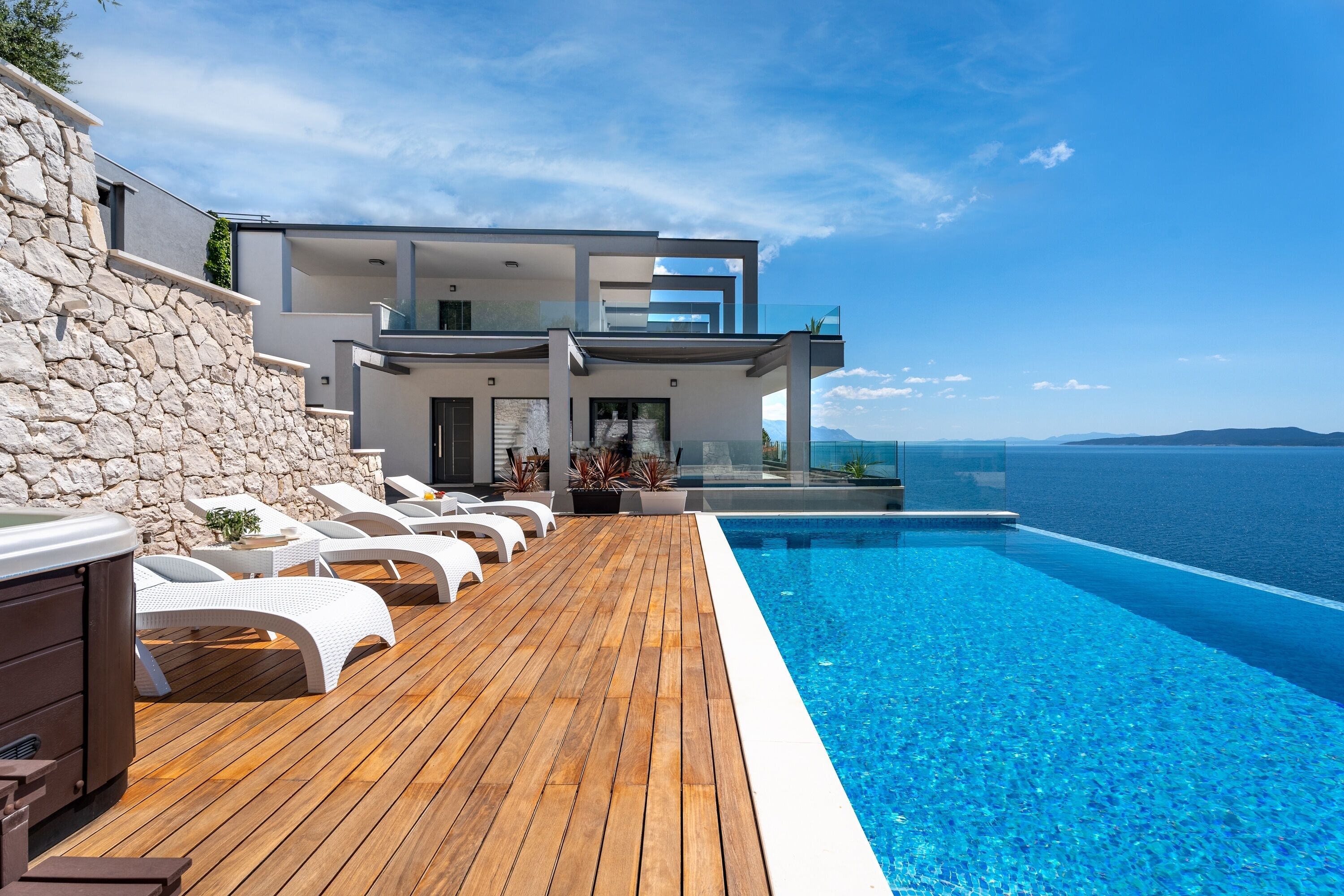 A modern villa with a wooden deck and a pool overlooking the sea.