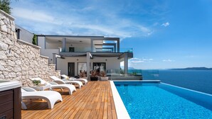 Une villa moderne dotée d’une terrasse en bois et d’une piscine offrant une vue sur la mer.