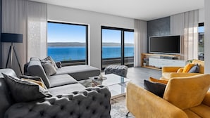 Un salon moderne doté d’un grand téléviseur à écran plat, d’un canapé, d’une table basse et offrant une vue sur la mer.