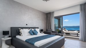 Une chambre moderne avec un grand lit, un balcon offrant une vue sur la mer et un coin salon avec une table et des chaises.