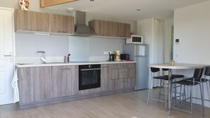 A modern kitchen with wooden cabinets, a built-in oven, a microwave, and a small dining area with stools.