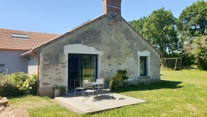 A rustic stone house with a tiled roof, a wooden deck, and a small patio area with a table and chairs.