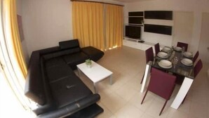 Una sala de estar con un sofá negro, una mesa de centro blanca y una zona de comedor con una mesa dispuesta para cuatro comensales.