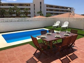 A swimming pool with a white fence, a dining table with chairs, and a building in the background. - BEAUTIFUL HOLIDAY HOME 84 WITH PRIVATE POOL (Callao Salvaje)
