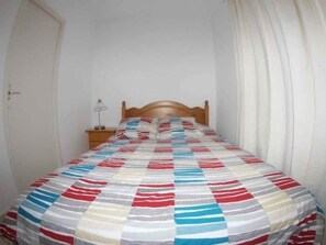A single bed with a striped bedspread, a wooden headboard, a nightstand with a lamp, and a white door.