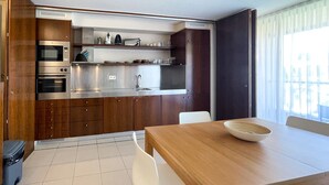 A modern kitchen with stainless steel appliances, wooden cabinets, and a dining area with a wooden table and white chairs. - Herdade dos Salgados, T1-10A-2D - Pool View, (Albufeira)