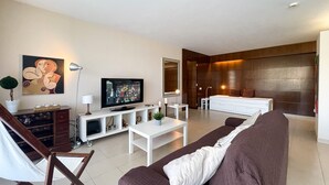 A modern living room with a flat-screen TV, a sofa, a coffee table, and a dining area with a white table and chairs. - Herdade dos Salgados, T1-10A-2D - Pool View, (Albufeira)