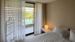 A hotel room with a bed, a nightstand with a lamp, and a view of a pool through sheer curtains. - Herdade dos Salgados, T1-10A-2D - Pool View, (Albufeira)