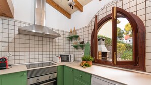A kitchen with green cabinets, a built-in oven, a microwave, and a dishwasher. There is a window with a wooden frame and a view of a house outside. - CAN TONI,  Apartment, 100 m from the white sand beach, for 6 People (Alcúdia)
