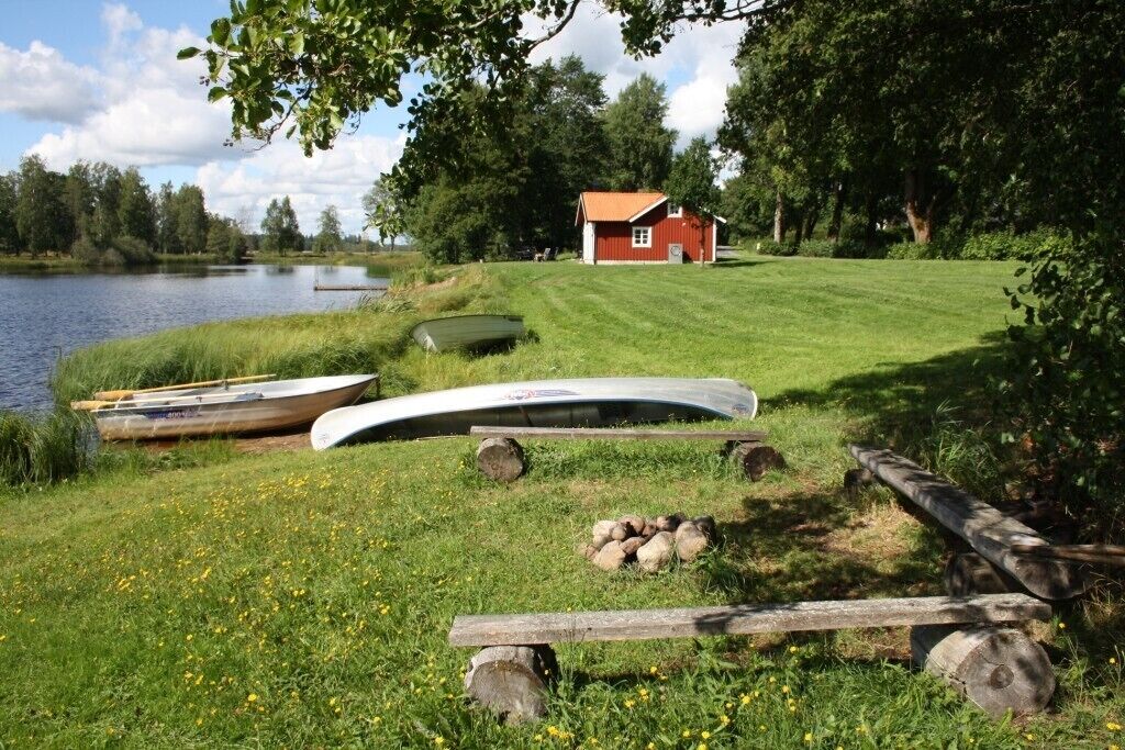 A lakeside scene with a red cabin, boats, and a grassy area.