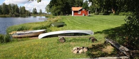 A lakeside scene with a red cabin, boats, and a grassy area.