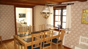 Un comedor con mesa y sillas de madera, una lámpara colgante y un ventanal con cortinas.