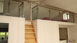 Una habitación con escalera de madera que sube a una zona superior con barandilla de vidrio.