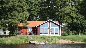 Una casa de fachada roja y amplias ventanas, ubicada junto a un cuerpo de agua con un muelle.