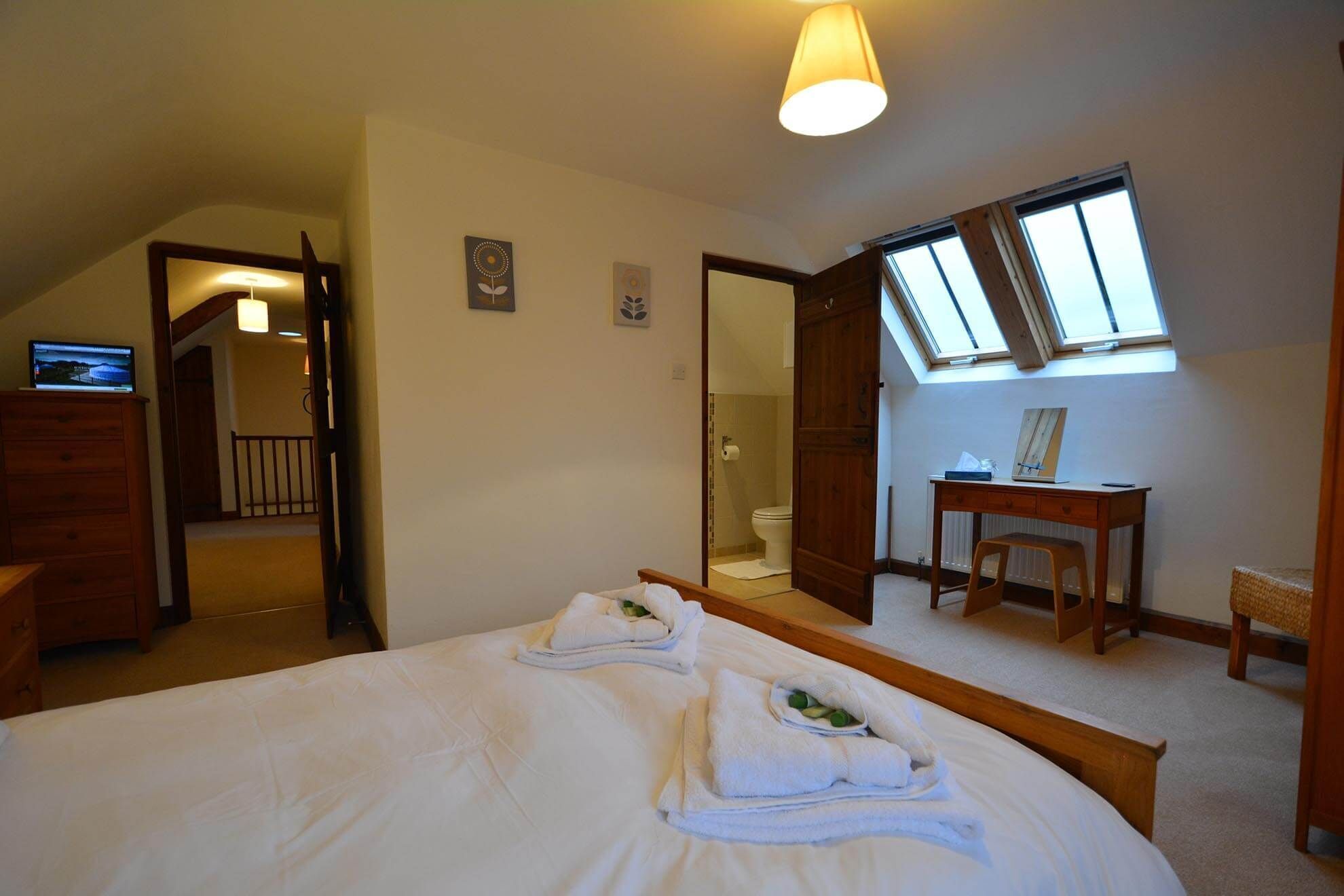Quarto com cama grande, escrivaninha, cadeira, espelho e claraboia.