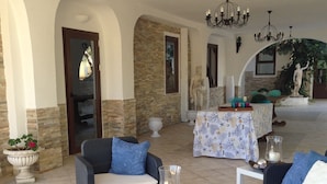 Un vaste espace extérieur aménagé avec des meubles en osier, une table recouverte d’une nappe à motifs floraux et une statue en arrière-plan.