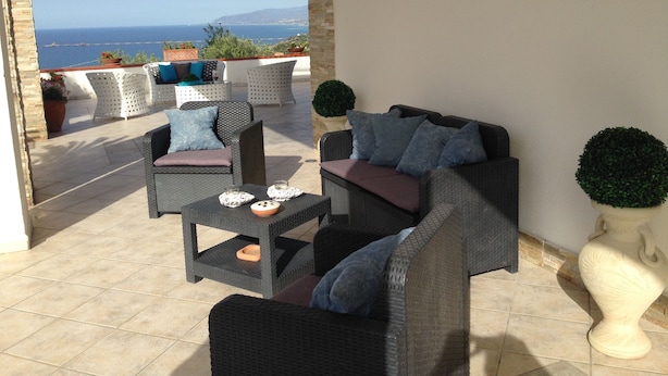 Une terrasse extérieure avec des meubles en osier, un vase blanc et une vue sur la mer.