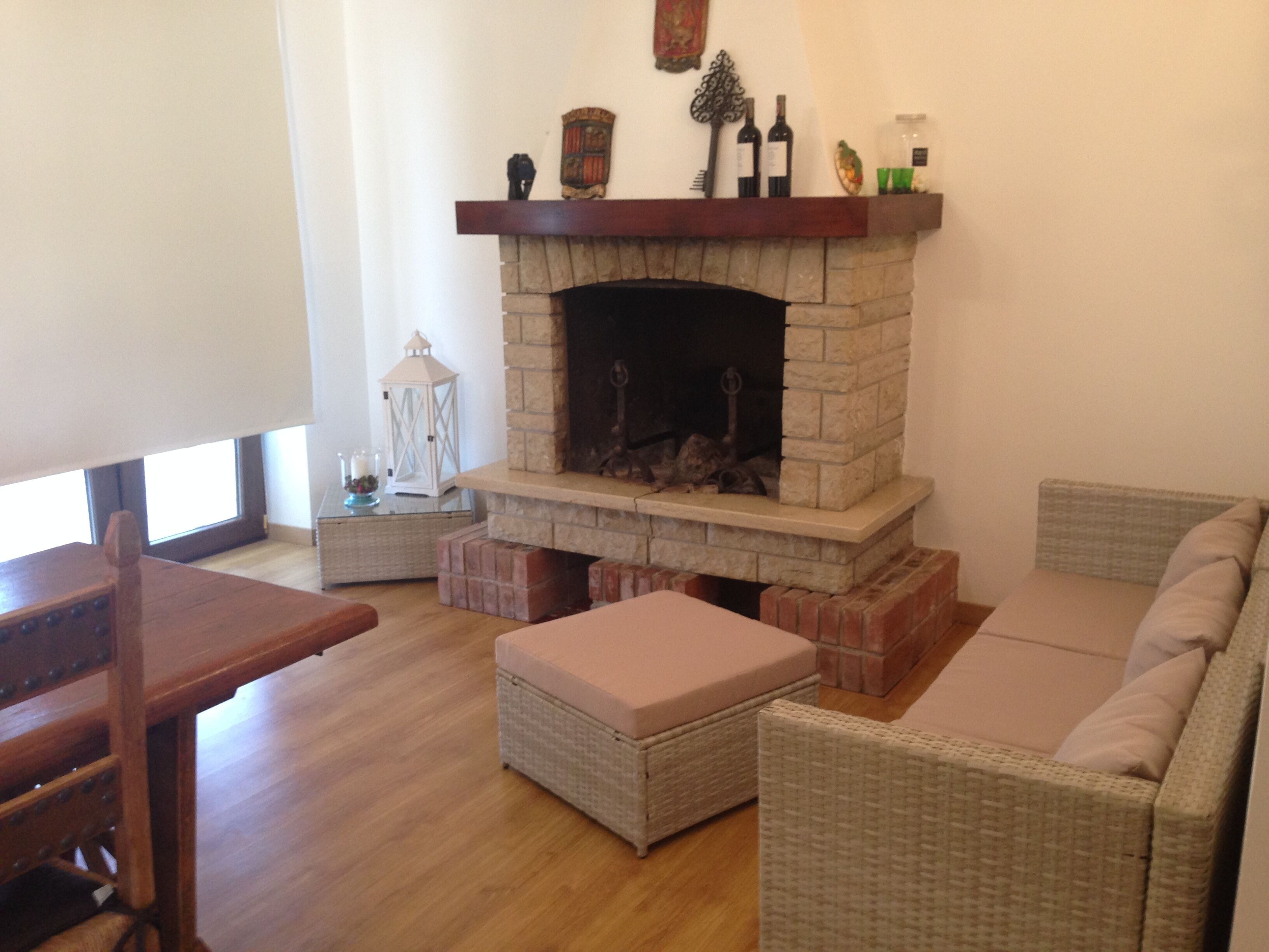 Ein Wohnzimmer mit Kamin aus Stein, Korbmöbeln und einem Holztisch.