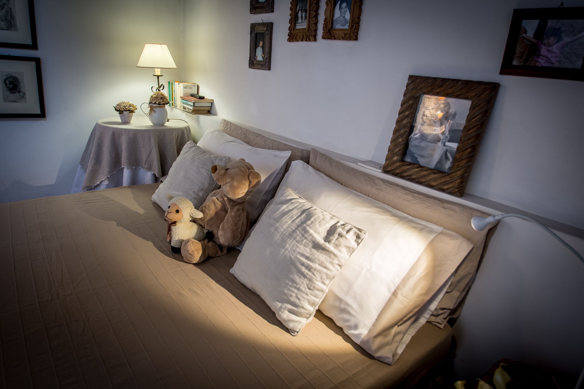 Un lit bien fait, avec des oreillers et un ours en peluche, une table de chevet avec une lampe et des photos encadrées accrochées au mur.