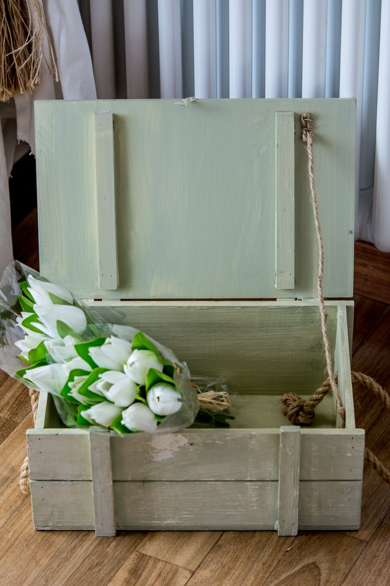 A rustic wooden chest with a rope handle, containing a bouquet of white flowers.