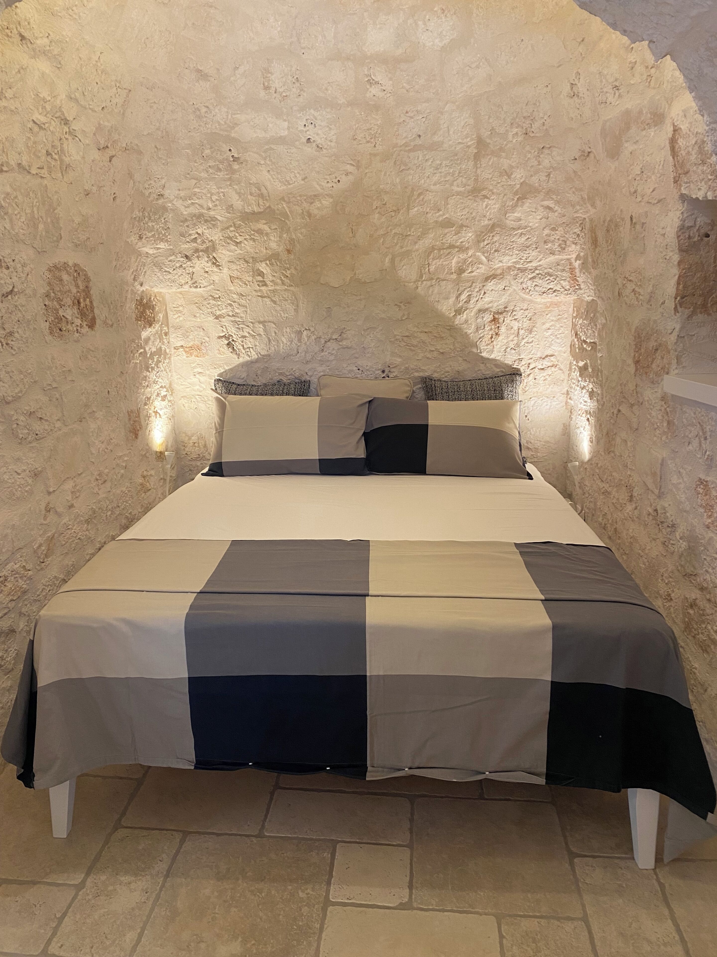 Ein Bett in einem Raum mit Steinsäulen und einer Bettdecke mit Schachmuster sowie Kissen.