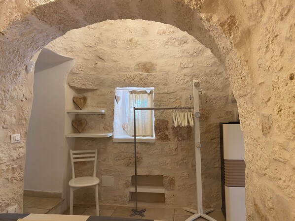 A rustic room with a stone wall, a window with a white curtain, a white chair, and a drying rack. - Perfect oasis among Olive Trees and Private Pool, for an authentic experience! (Ostuni)