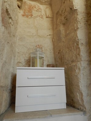 A dresser with two drawers stands against a stone wall, topped with a lantern.