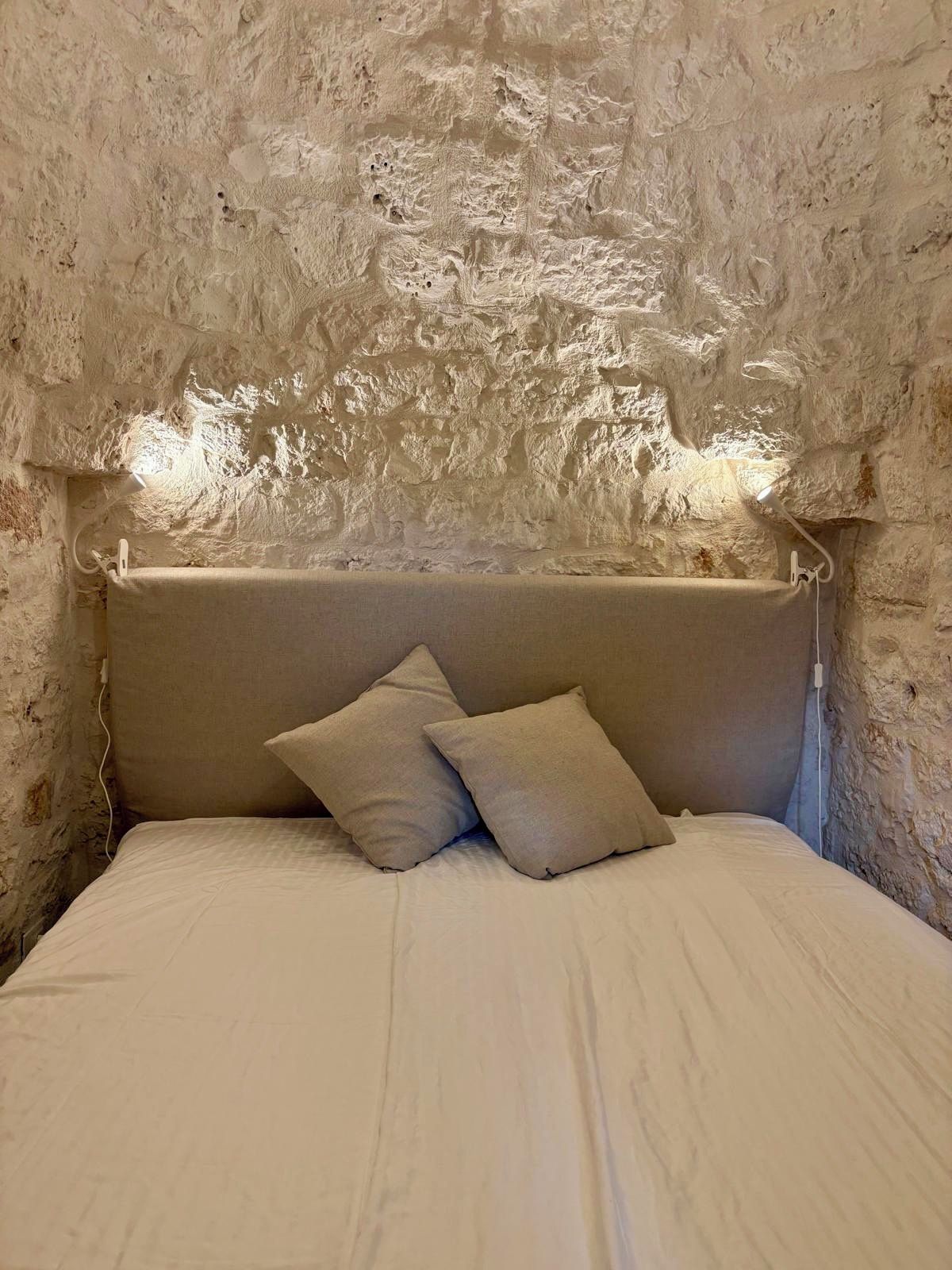 A bed with a headboard against a textured stone wall.
