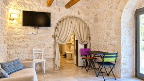 Une pièce aux murs de pierre, équipée d’un téléviseur à écran plat, d’un canapé, d’une table avec des chaises et d’une fenêtre.