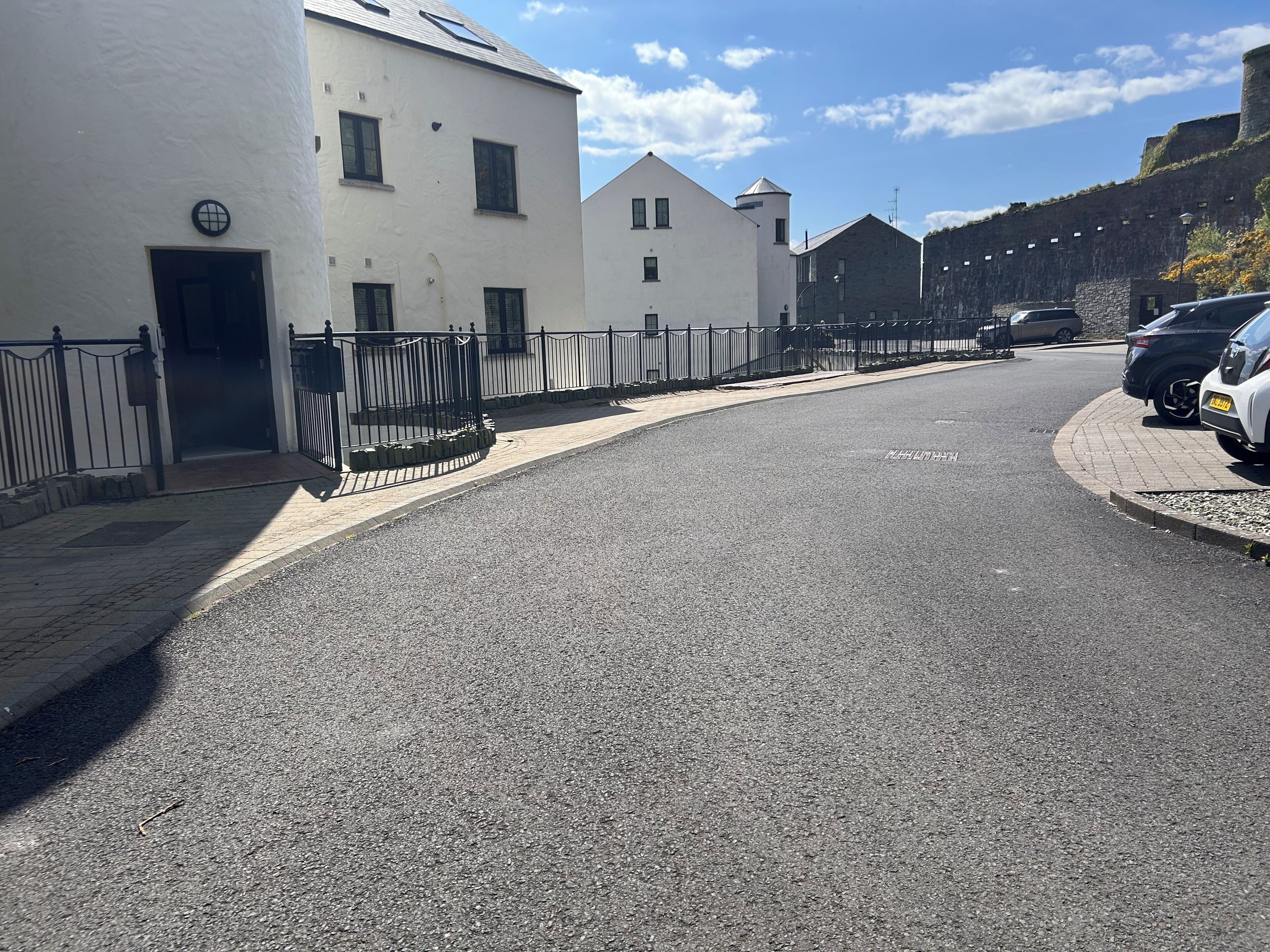 Une rue bordée d’un immeuble blanc, d’une entrée fermée par un portail et de voitures garées.