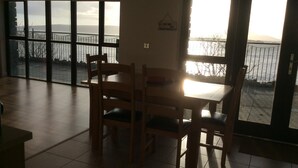 Una habitación con una mesa de comedor y sillas, ventanas amplias con vistas al mar y a un puente, y un cartel en la pared.
