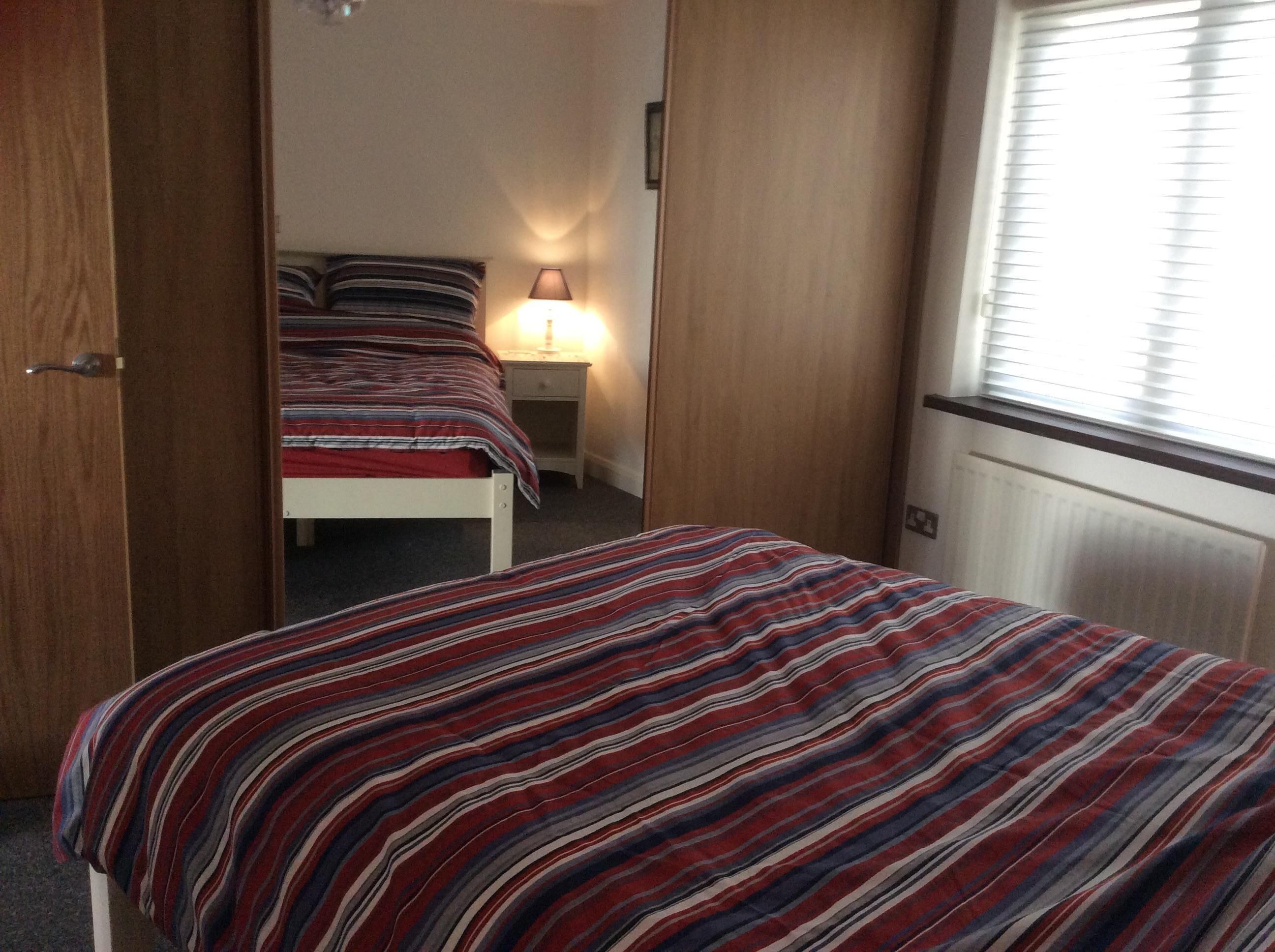 Une chambre à coucher avec un lit, une table de chevet, une lampe et une fenêtre avec des stores.