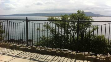 A stone-paved walkway with a metal railing overlooking a body of water and distant mountains.
