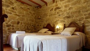 Una habitación con dos camas, vigas de madera, paredes de piedra y una mesita de noche con lámpara.