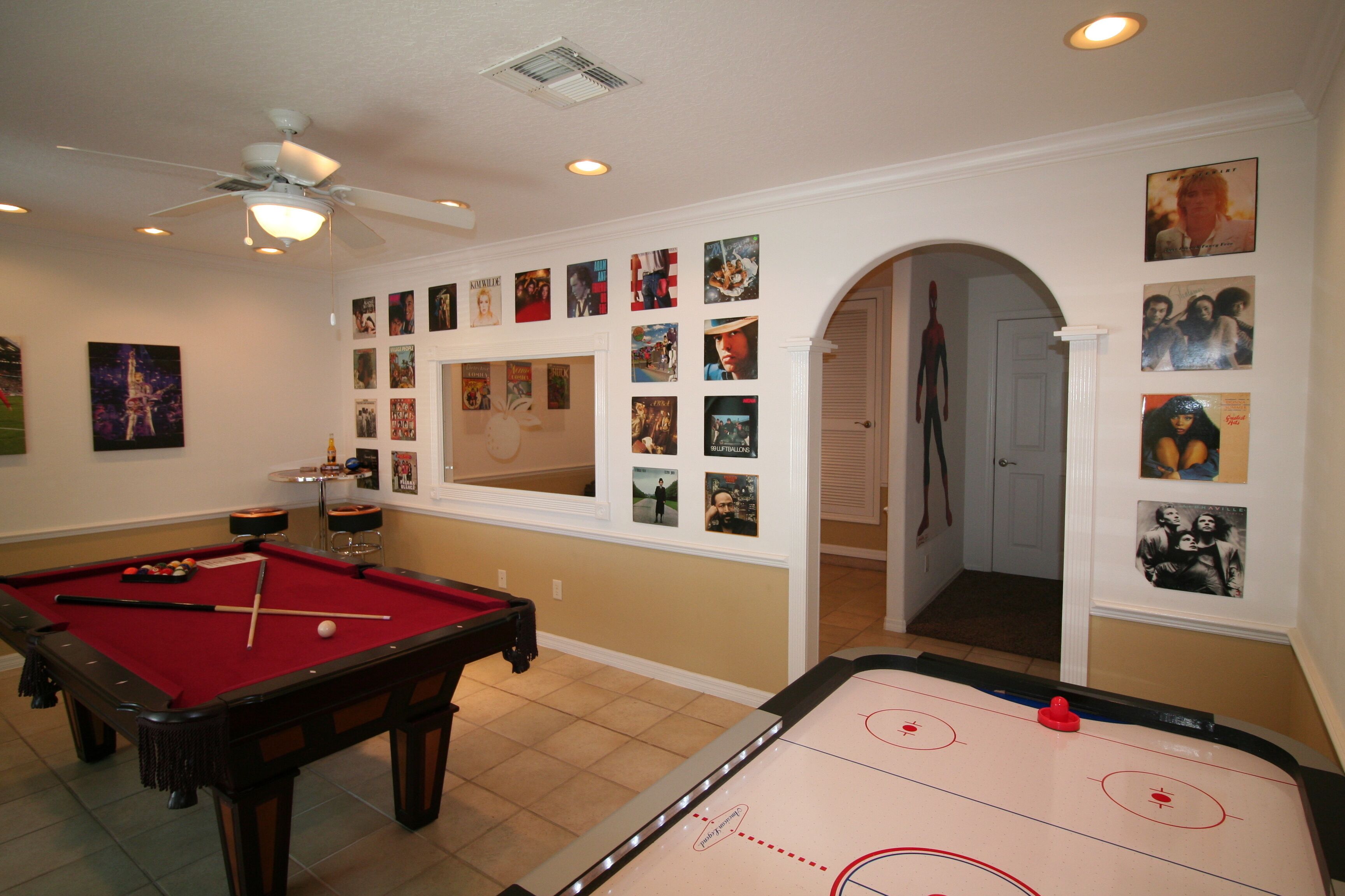 A room with a pool table, a foosball table, and a wall decorated with various posters.