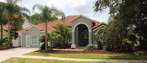 A residential house with a red roof, a front entrance with an arched doorway, and a well-maintained lawn with palm trees.