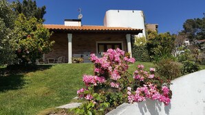 Ein Haus mit Backsteinfassade und Ziegeldach. Auf dem Dach befindet sich ein weißer Tank. Im Vordergrund befindet sich ein Garten mit rosa Blüten.