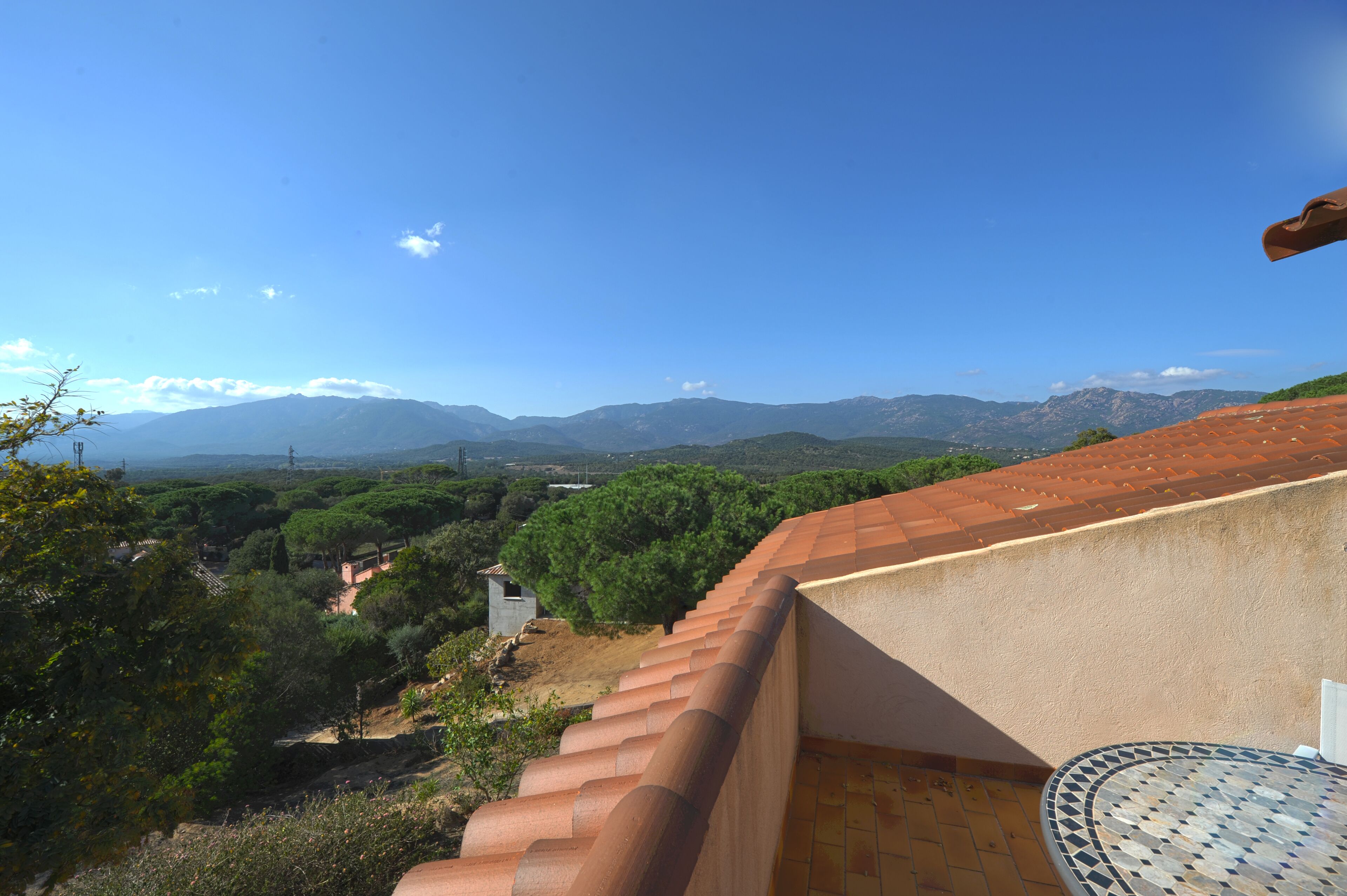 A terrace with a view of mountains, a tiled table, and a red roof.