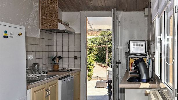 A compact kitchen with a dishwasher, a coffee maker, and a view of a garden through an open door.