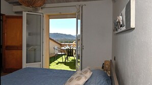A bedroom with a bed, a window, and a view of a balcony with a table and chairs.