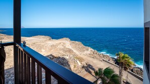 Blick auf die Küste vom Balkon mit felsiger Uferlinie, Meer und Palmen.