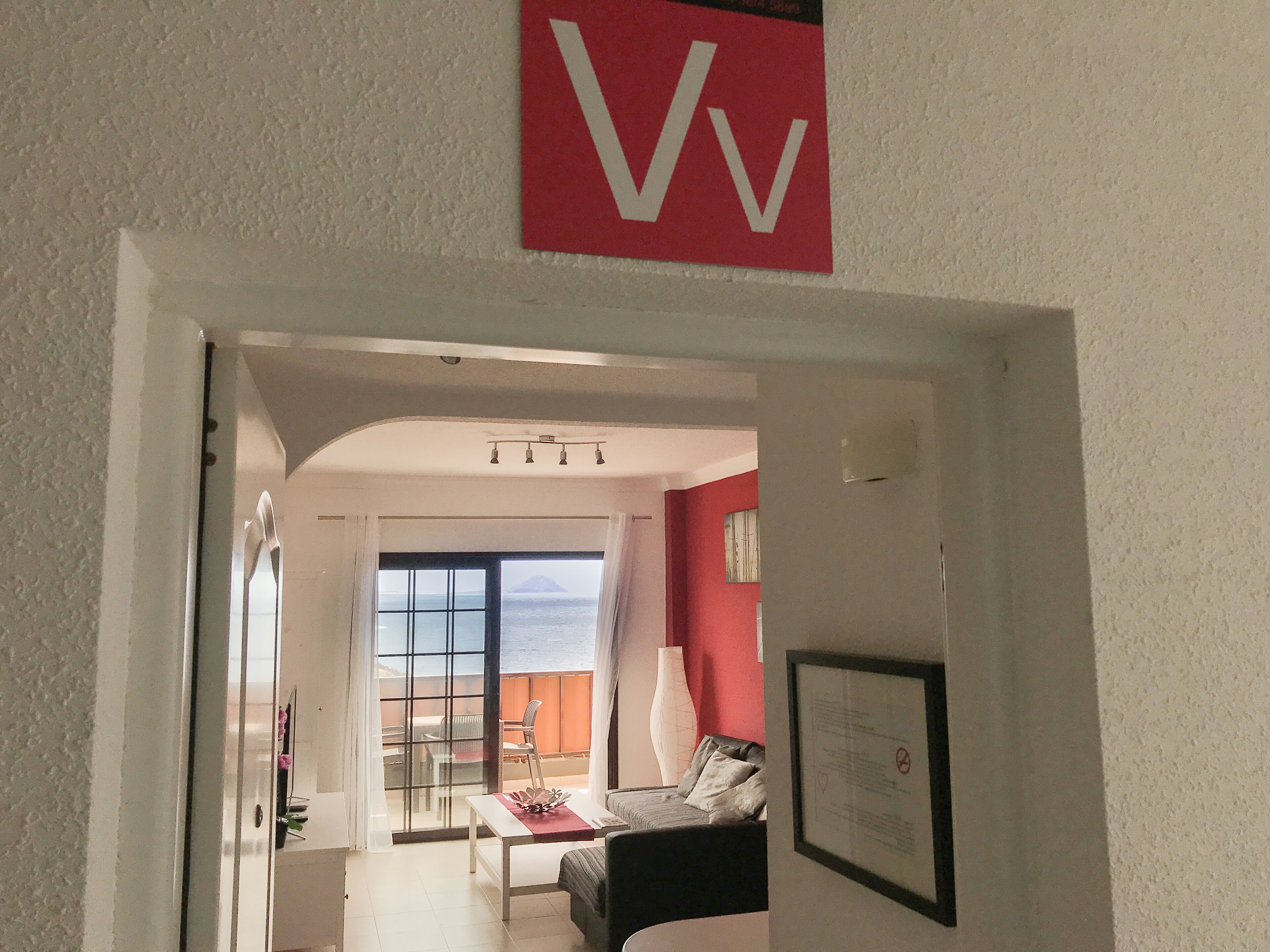 Een woonkamer met uitzicht op zee, een rode wand en een lijst met een bericht aan de wand.