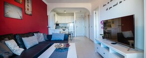 A modern living room with a sofa, a coffee table, and a TV. There is a kitchen visible in the background. - 1st LINE of sea | Free private WIFI | international TV channels (Arona)