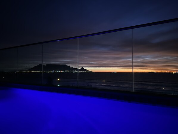 Vista noturna de uma varanda, com o horizonte da cidade e montanhas ao longe.